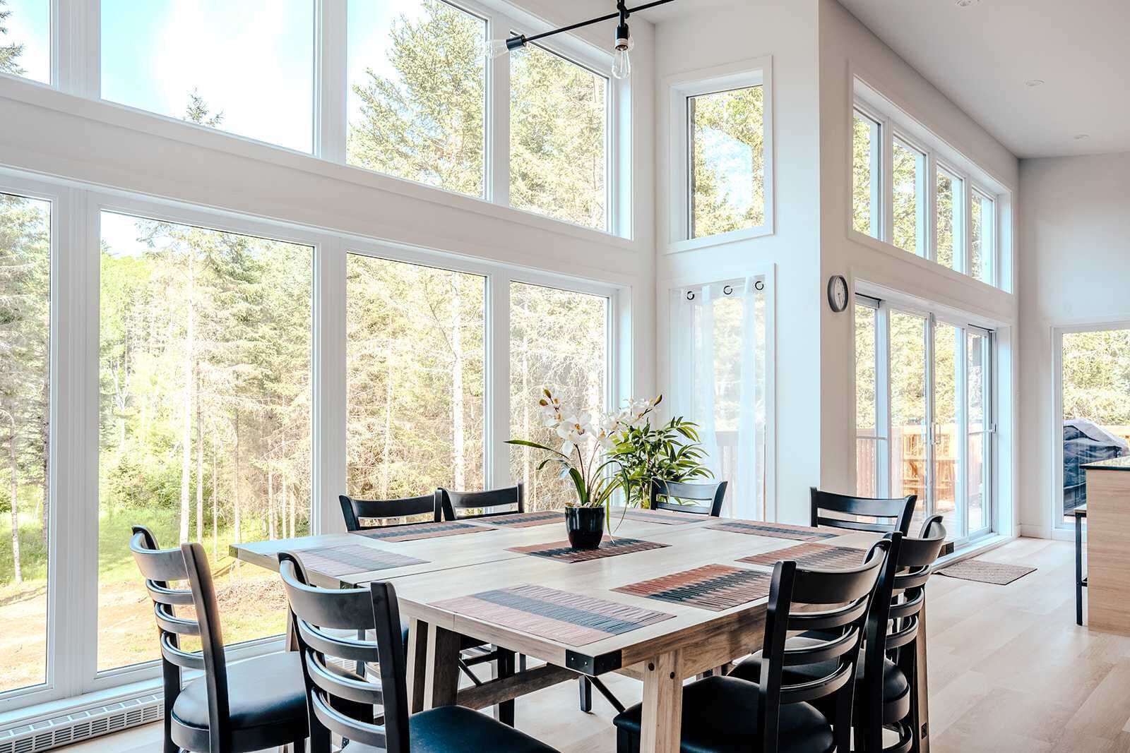 A dining area with a large table, chairs, and a view of trees through large windows.