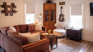 A living room with a brown leather sofa, a white armchair, a wooden cabinet, and a guitar on the wall.