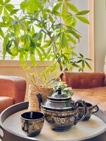 Uma mesa redonda com um conjunto de chá, uma cesta de vime e uma planta em vaso.
