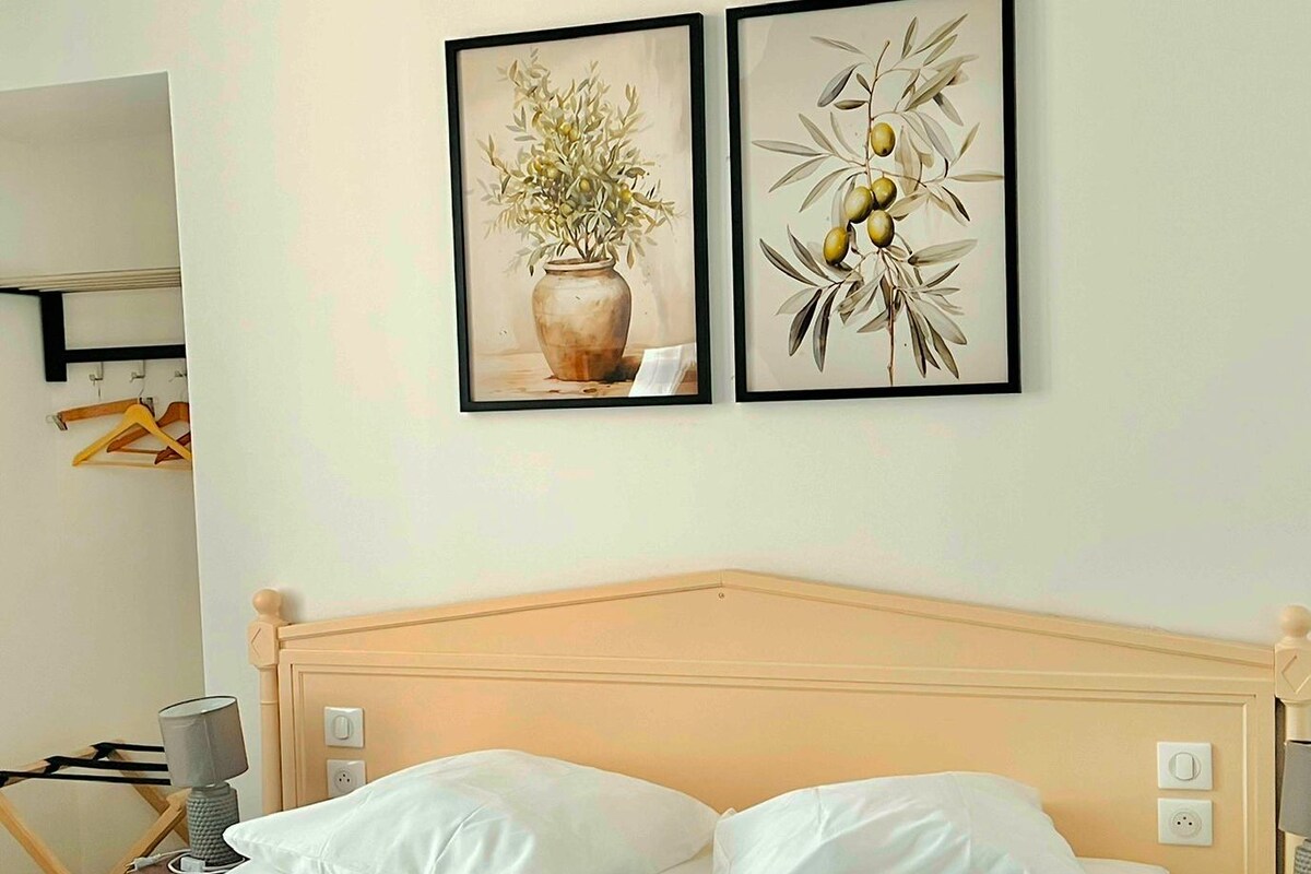 Quarto de hotel com uma cama, duas obras de arte emolduradas, cabeceira de madeira e mesa de cabeceira com abajur.