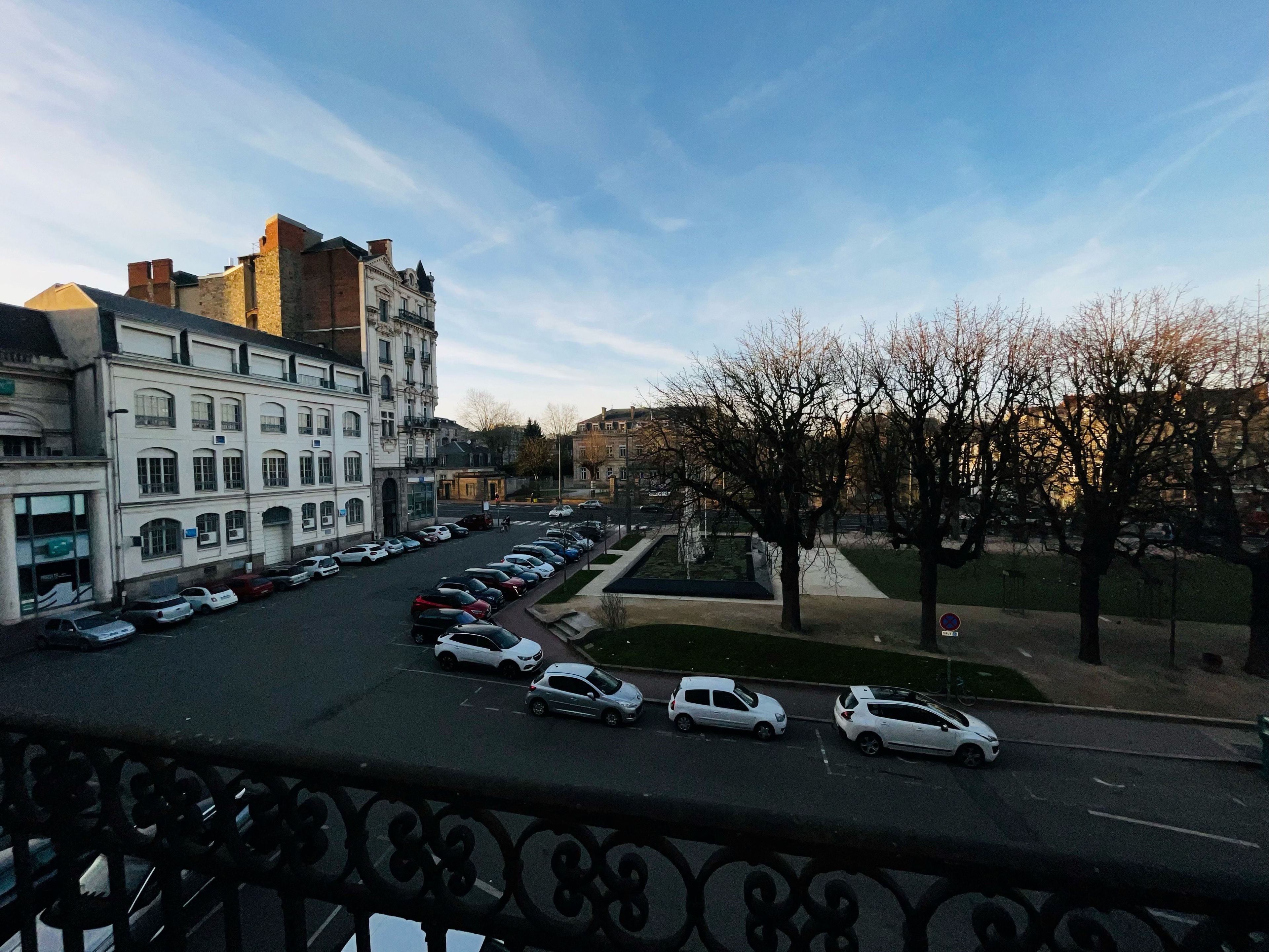 A city street with parked cars, buildings, and a clear sky.