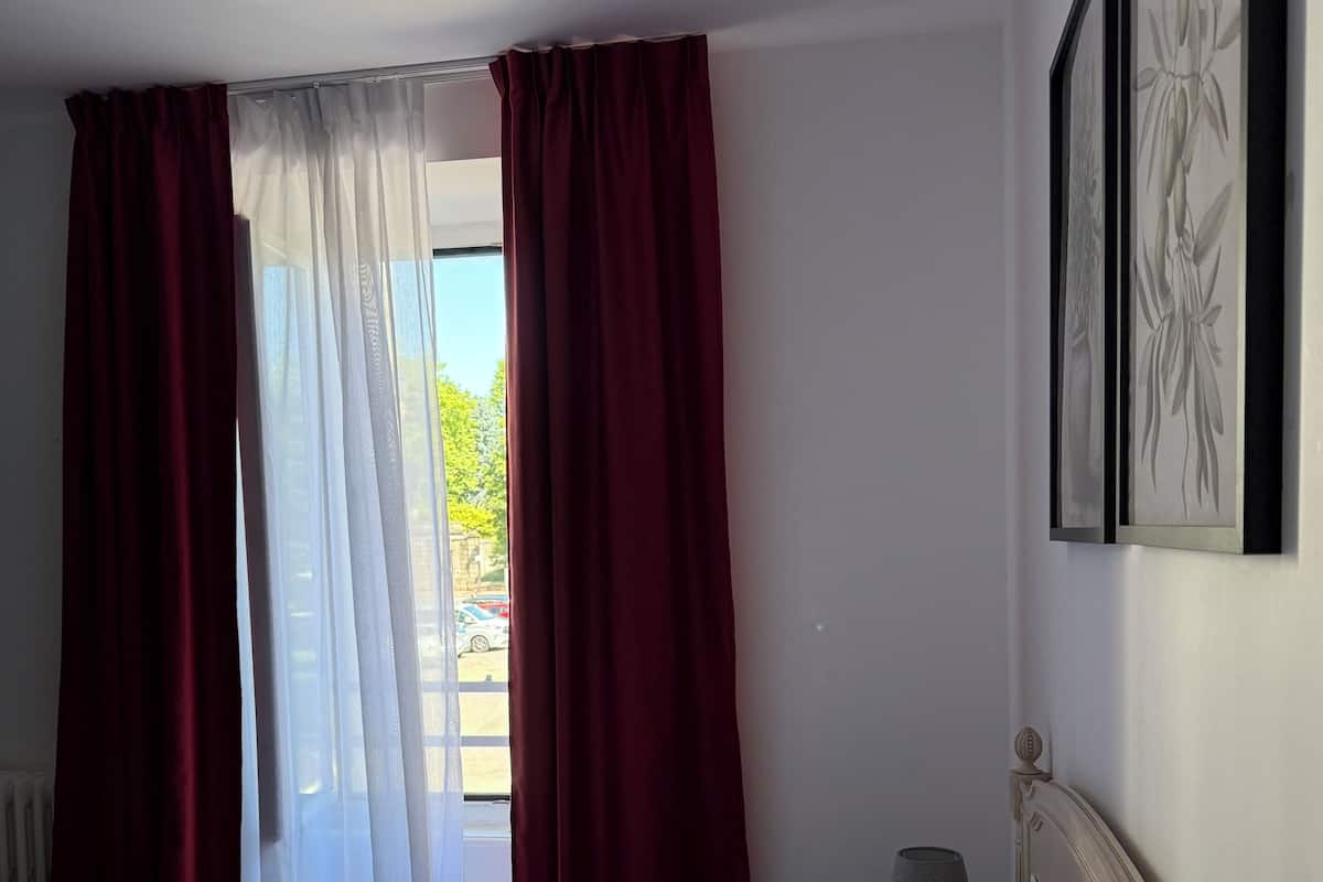 A hotel room with two beds, a window with red curtains, and a framed picture on the wall.