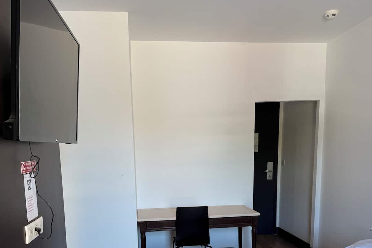 A hotel room with a bed, a desk, a chair, and a television mounted on the wall.