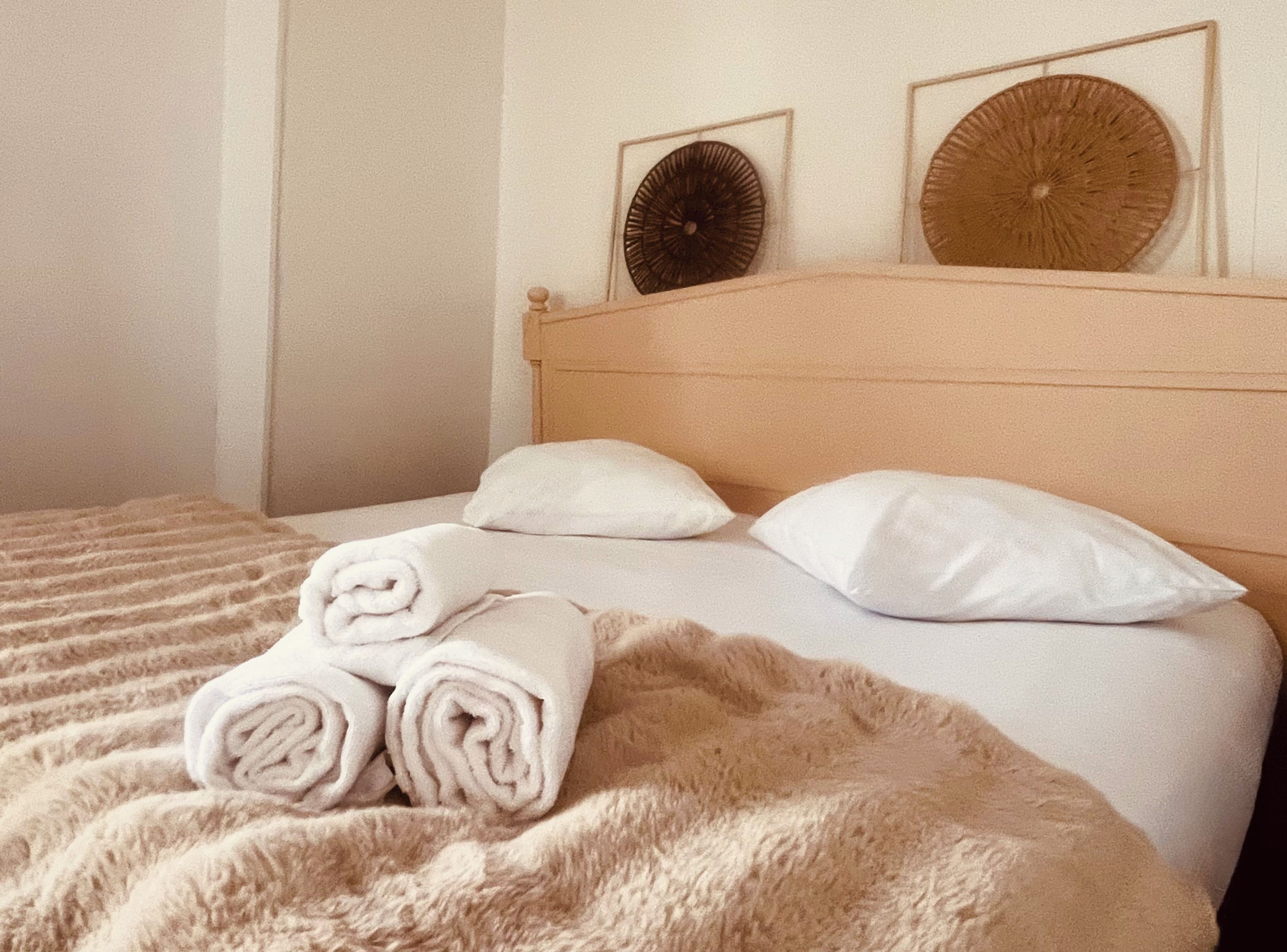 Un lit avec une couverture moelleuse, deux oreillers et des serviettes enroulées.