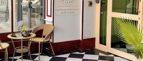 Entrada de hotel con piso a cuadros, muebles de mimbre y un cartel de bienvenida.
