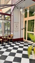 Entrada de hotel com piso xadrez, mobiliário de vime e placa de boas-vindas.