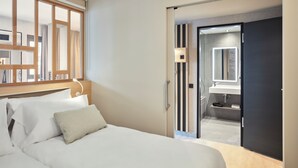 A hotel room with a bed, a bedside lamp, a wardrobe, and a bathroom visible through an open door.