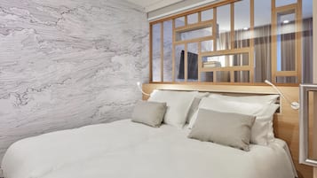 A neatly made bed with white linens and two pillows, a wooden headboard, and a wall with a marble-like pattern.