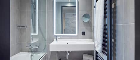 A modern bathroom with a glass-enclosed shower, a white sink with a marble backsplash, and a towel rack.