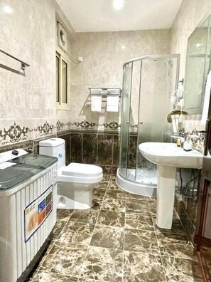 Une salle de bain comprenant des toilettes, un lavabo, un espace douche et une porte en verre.