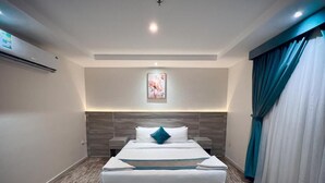 A modern hotel room with a large bed, a headboard with built-in lighting, a wall-mounted air conditioner, and a window with curtains. - Jawharat Alalia Hotel Apartments (Madinah)