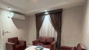 A modern living room with a sofa set, a coffee table, and a large window with curtains. - Jawharat Alalia Hotel Apartments (Madinah)