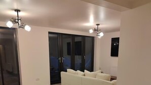 Ein geräumiges Zimmer mit einem großen weißen Sofa, einem Deckenventilator und einer Schiebetür zum Balkon.