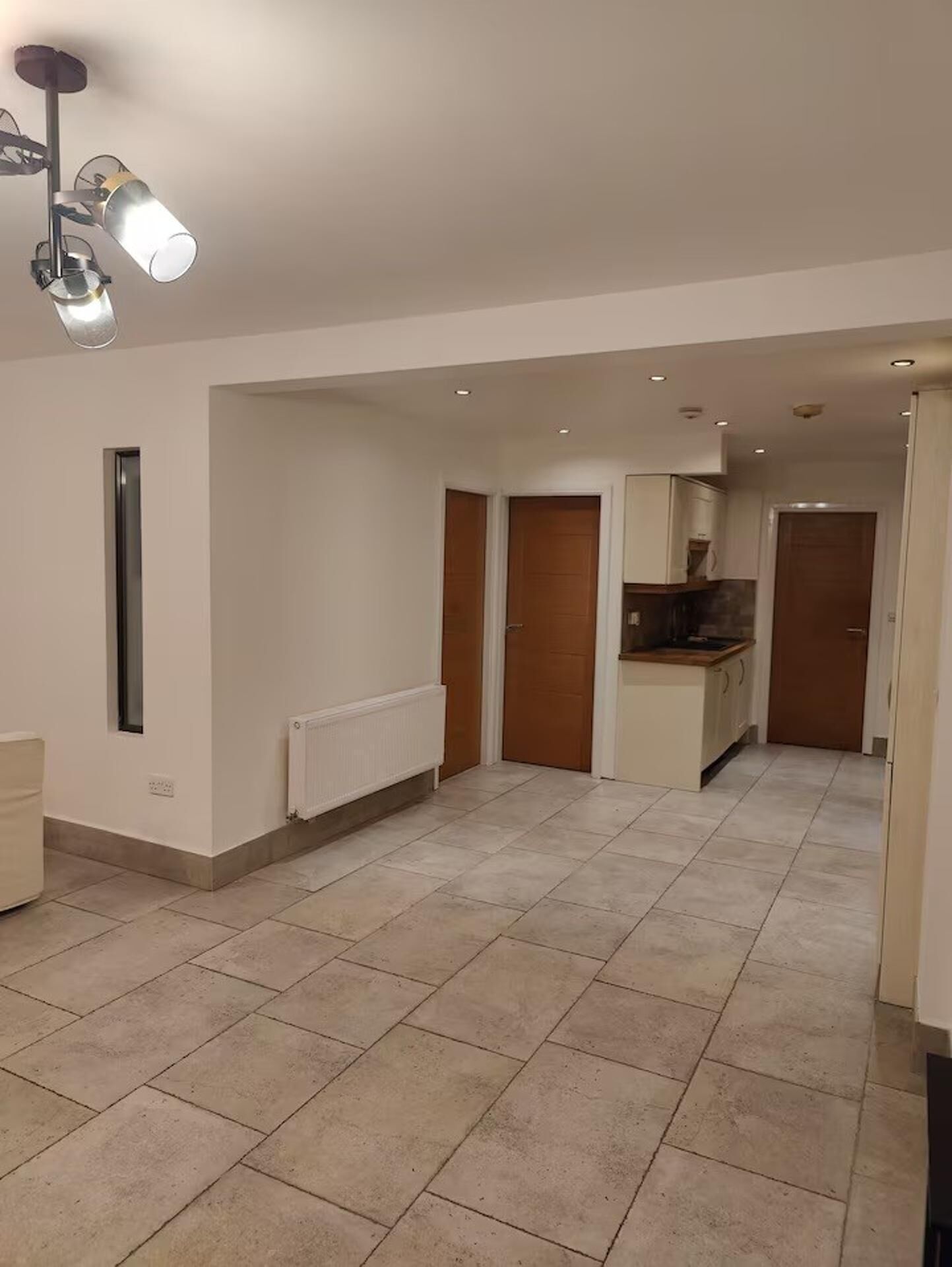 A spacious living area with a kitchen in the background, a radiator, and a ceiling light fixture.