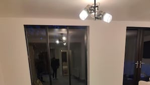 Ein geräumiger Raum mit Fliesenboden, einer Schiebetür zu einem abgedunkelten Gang und einer Deckenleuchte.