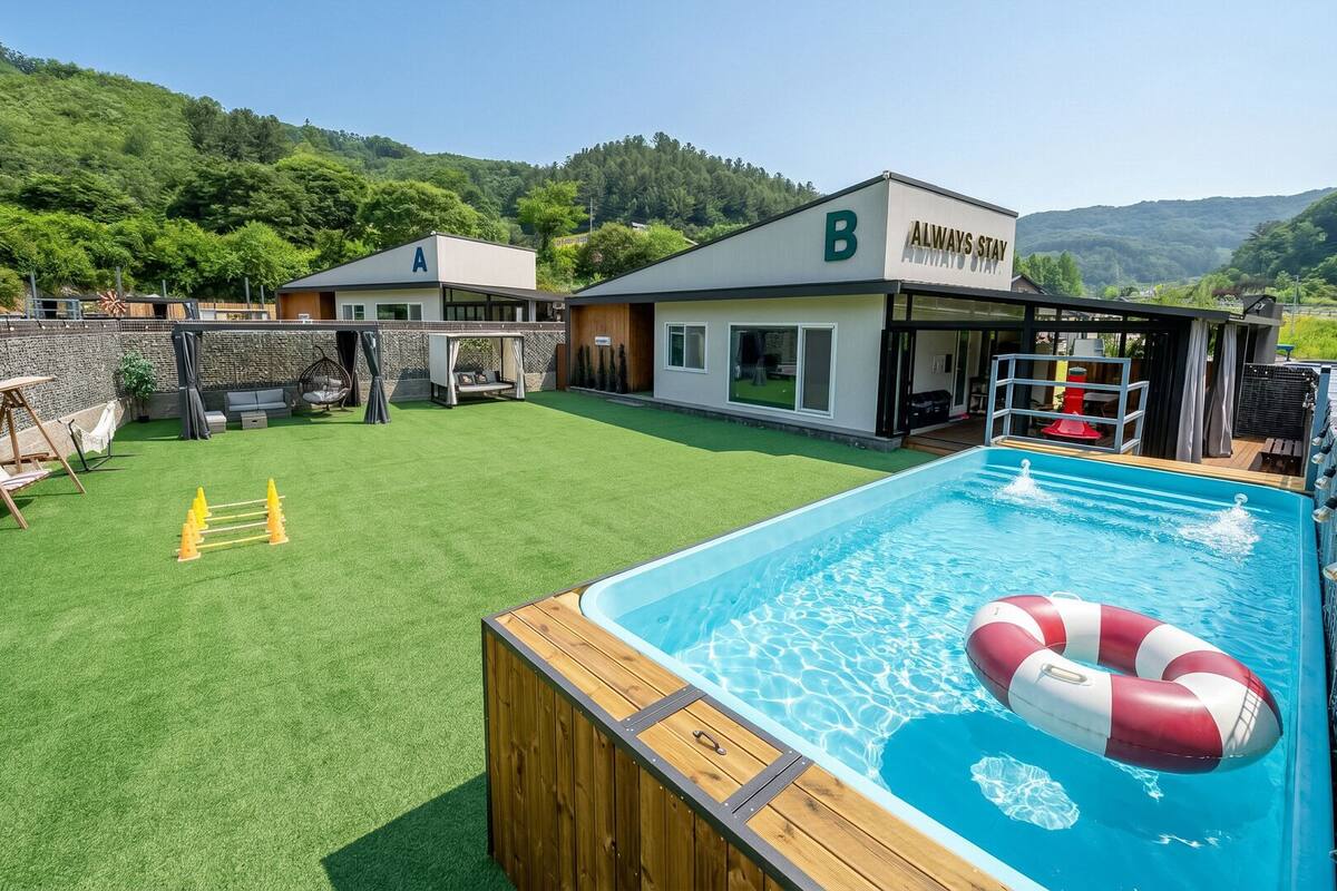 Zona de piscina con terraza de madera, un flotador salvavidas y vista a un edificio con el letrero 'ALWAYS STAY'.