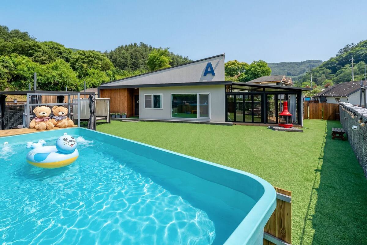 Una piscina con juguetes inflables, un área cercada y una casa con un letrero que dice 'A'.