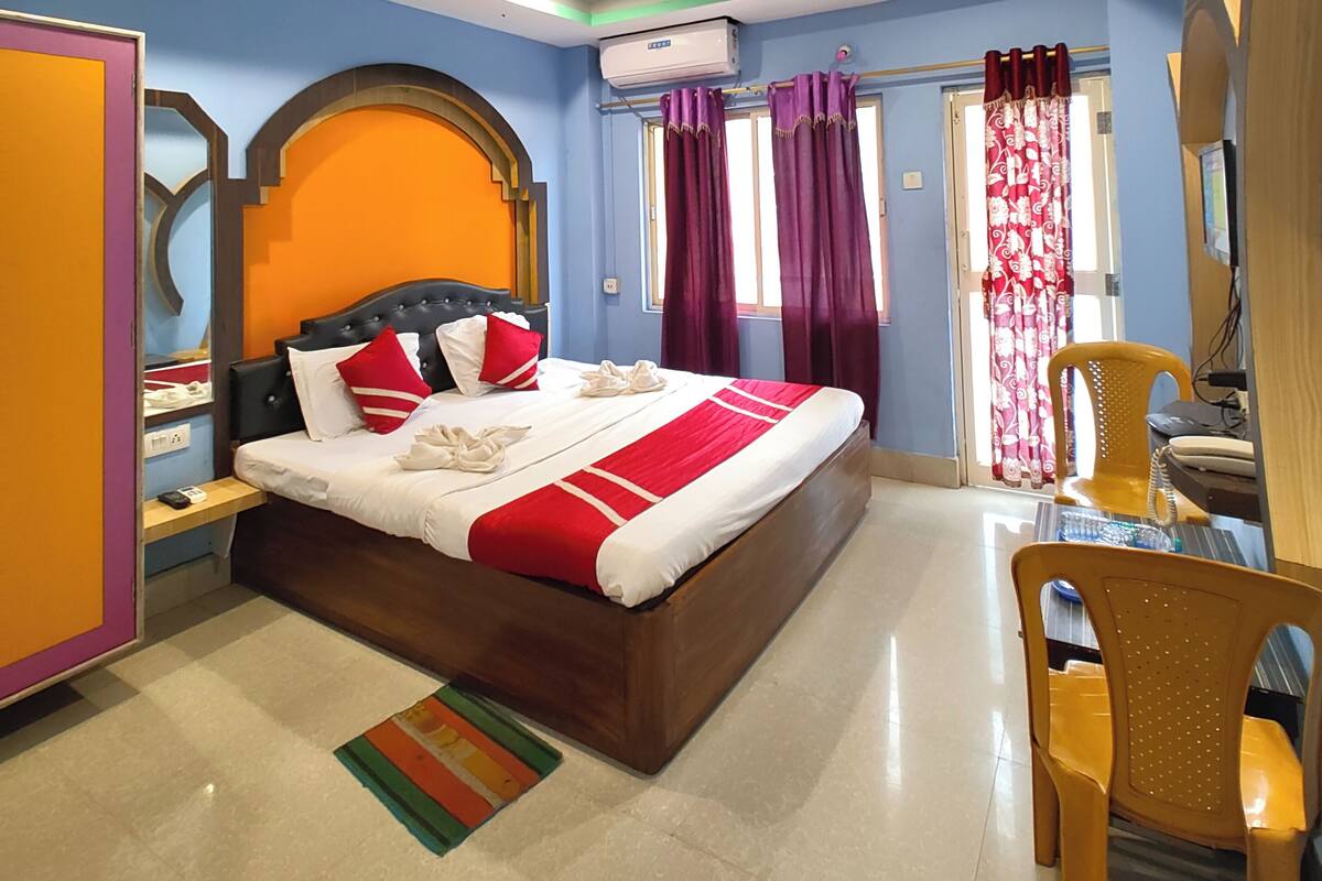 Une chambre d’hôtel avec un grand lit, un bureau avec une chaise, une armoire et une salle de bain visible à travers une porte ouverte.