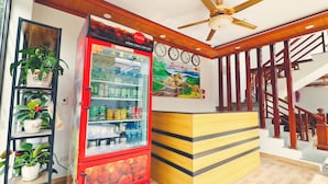 A reception area with a Coca-Cola refrigerator stocked with beverages, a wooden reception desk, a staircase, and a ceiling fan. - Tam Coc Homestay Thanh Thang (Nam Hoa Lu)