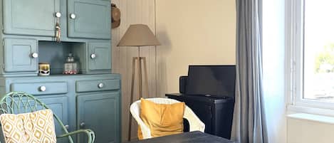 A room with a blue cabinet, a wicker chair, a table, a lamp, and a television.
