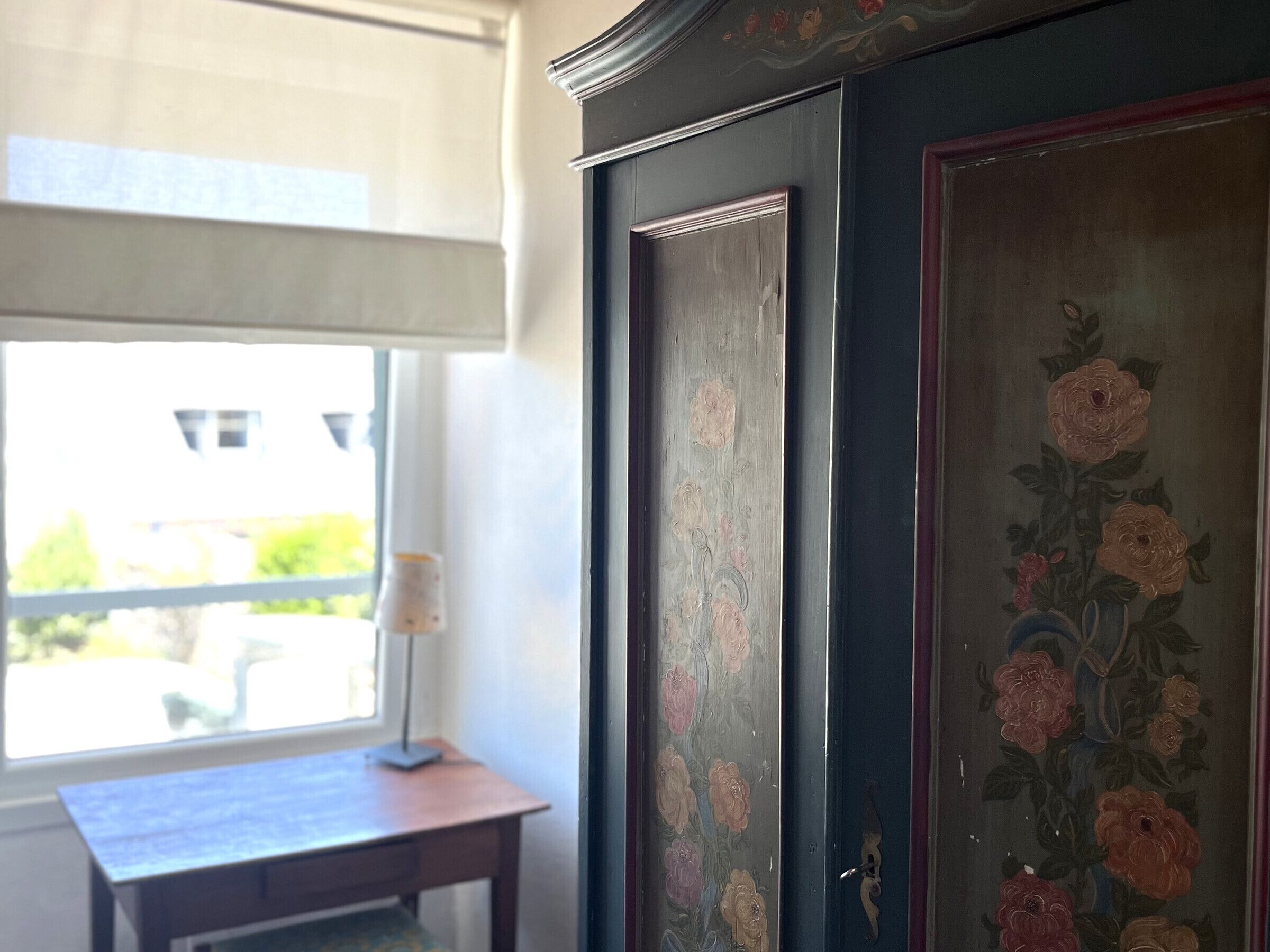 Una habitación con ventana, escritorio y puerta decorada con motivos florales.