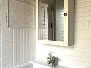 Ein Badezimmer mit weiß gefliester Wand, einem Spiegel über einem Waschbecken und einer Handseifenflasche.