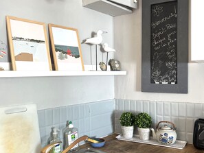 A kitchen with a chalkboard displaying a welcome message, framed artwork, and decorative items.