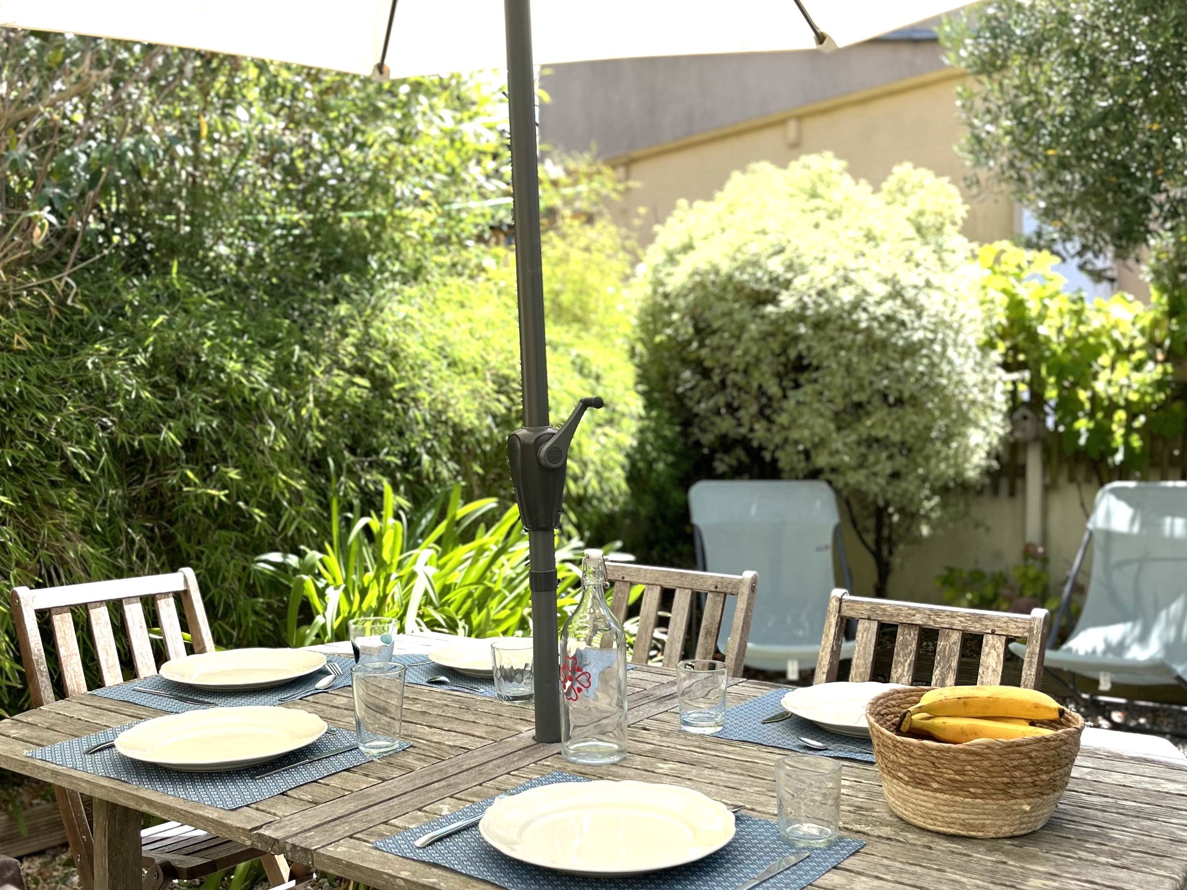 An outdoor dining area with a table set for two, surrounded by greenery and a clear sky.