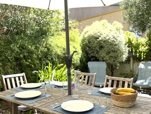 Un espace de restauration en plein air avec une table dressée pour deux personnes, entouré de verdure et sous un ciel dégagé.