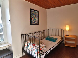 Ein Einzelbett mit Metallgestell, ein Nachttisch mit Lampe und ein Fenster mit Blick.