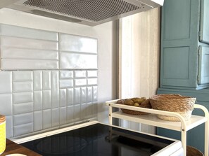 A kitchen with a white tiled backsplash, a microwave, a white metal shelf with baskets, and a window with a view.