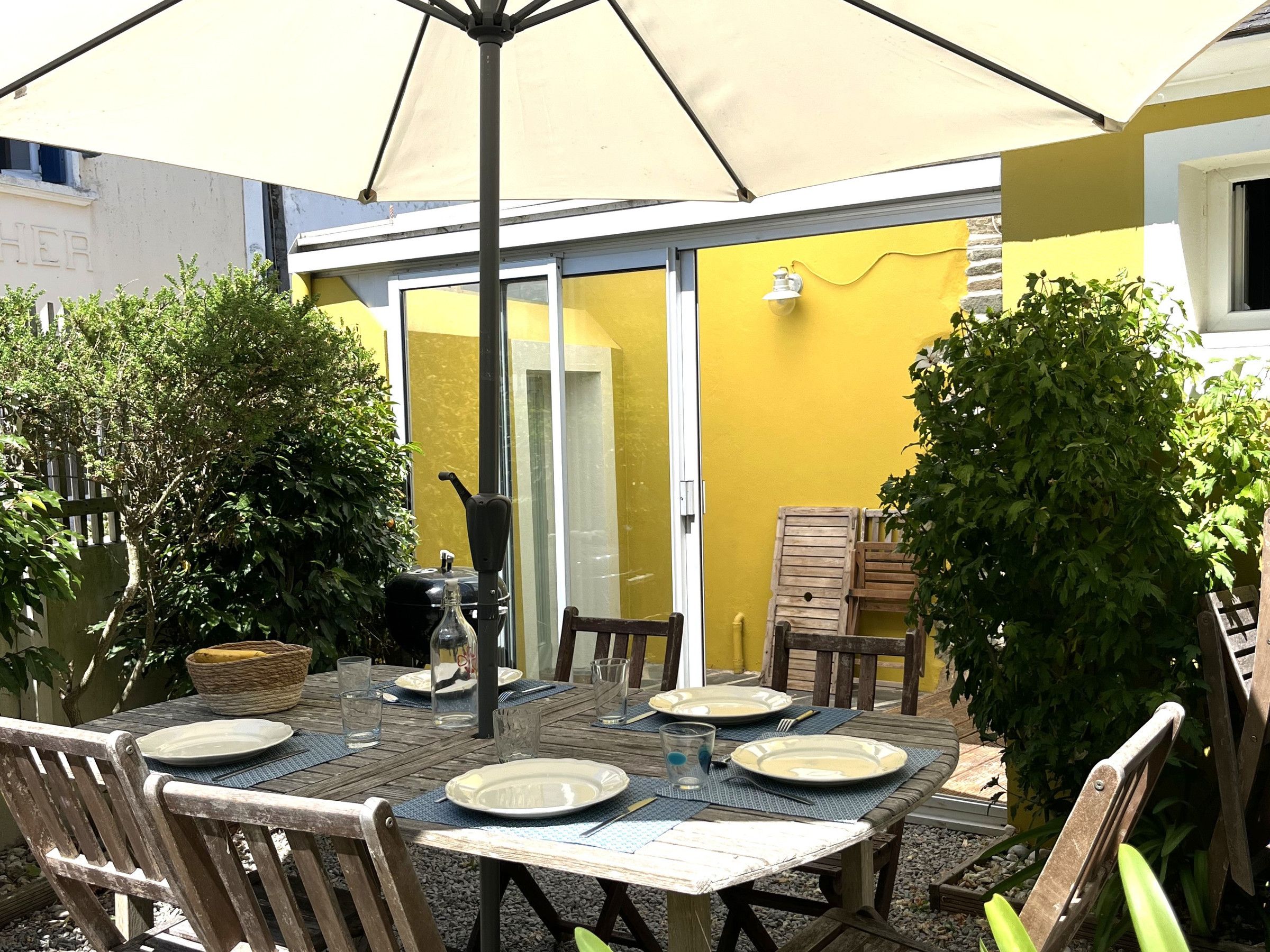 Ein Essbereich im Freien mit einem Tisch für vier Personen, umgeben von Stühlen, unter einem großen Sonnenschirm.