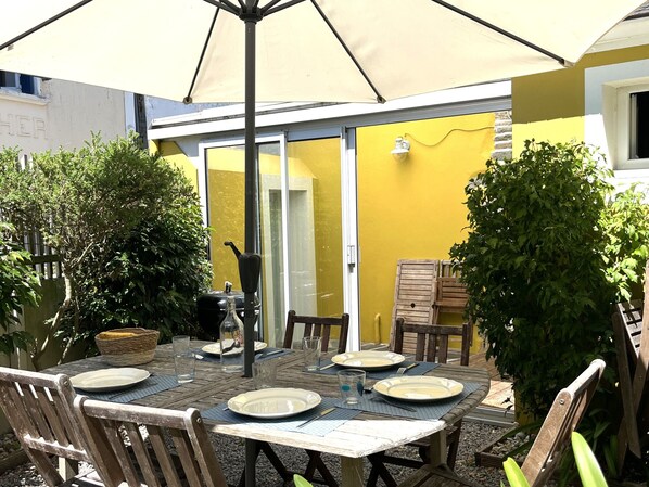 Ein Essbereich im Freien mit einem Tisch für vier Personen, umgeben von Stühlen, unter einem großen Sonnenschirm.