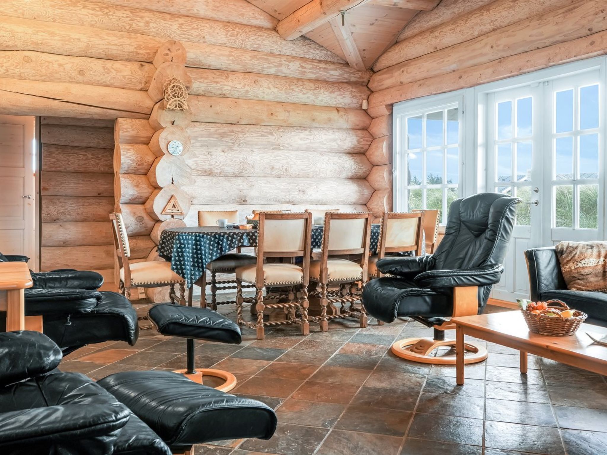 Interior d'una cabana de fusta amb zona de dinar, seients de pell i una finestra gran.