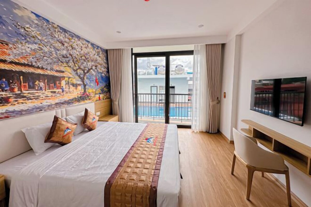 Ein Hotelzimmer mit Bett, Schreibtisch, Fernseher und einem Balkon mit Blick auf einen Pool.