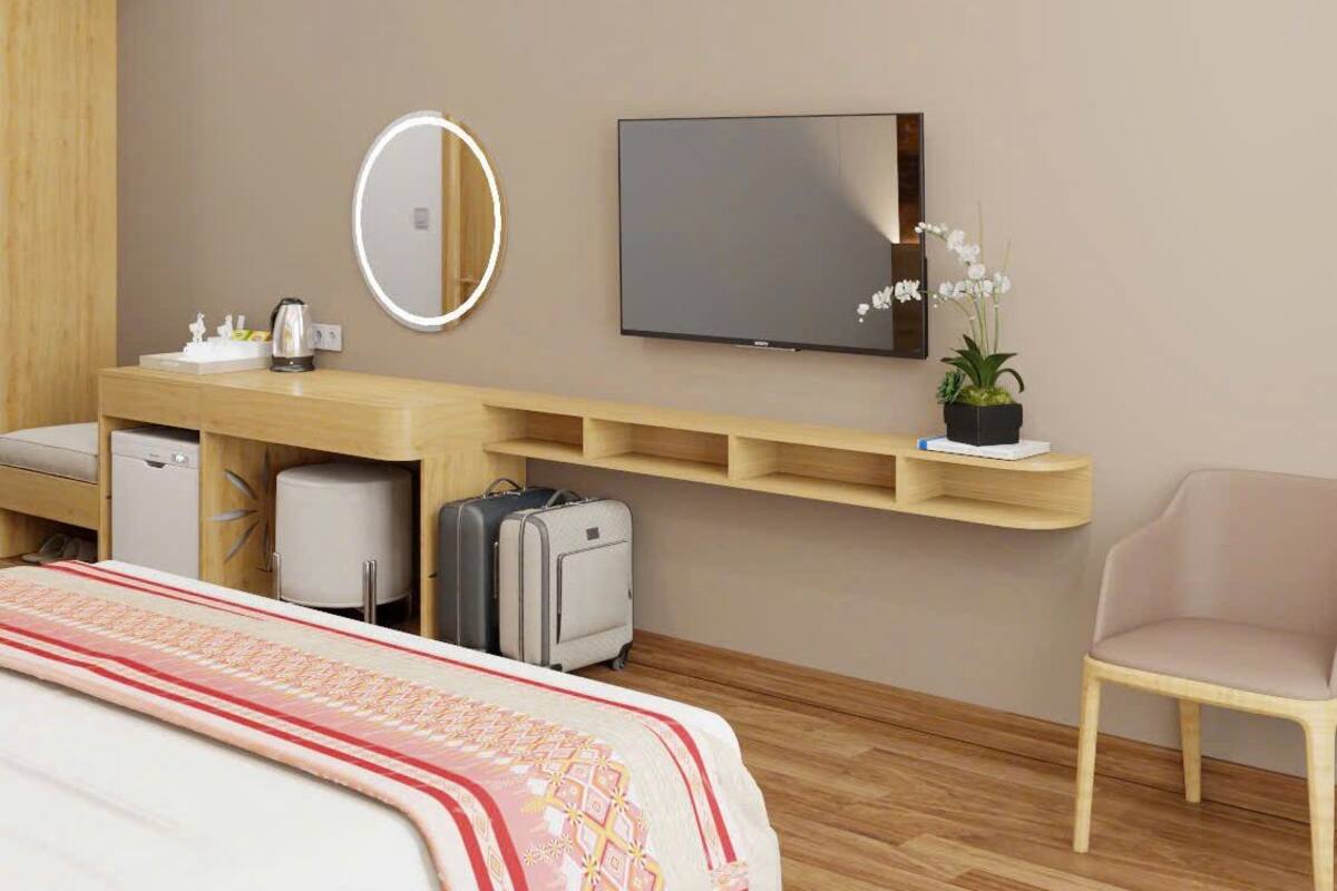 Quarto de hotel com cama, escrivaninha com espelho, televisão, cadeira e uma pequena planta em vaso.