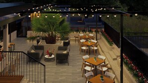 Un espace extérieur aménagé avec des tables et des chaises, une grande plante centrale et des guirlandes lumineuses.