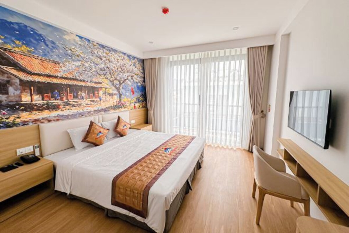 Habitación de hotel con una cama grande, un escritorio, una silla, un televisor y un mural en la pared.