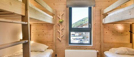 A dormitory room with bunk beds, a window with a view of a mountain, and a radiator.