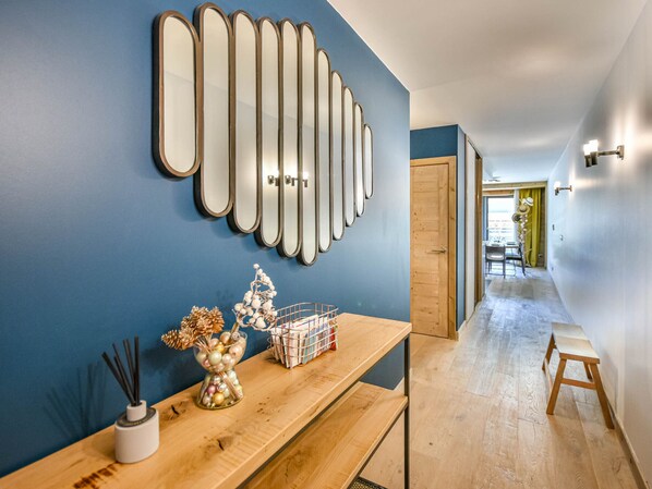 Un couloir avec un banc en bois, un miroir fixé au mur et un vase décoratif contenant des fleurs séchées.