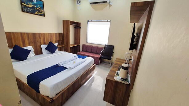 A hotel room with a large bed, a sofa, a TV, and a window with blinds. - RK Residency (Vrindavan)