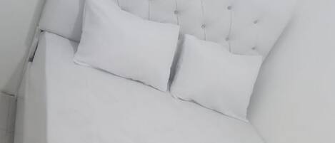 Una cama blanca con cabecera capitonada y dos almohadas.