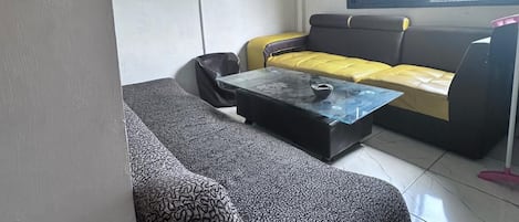 A modern living room with a sofa, a coffee table, and a window with a view of greenery.