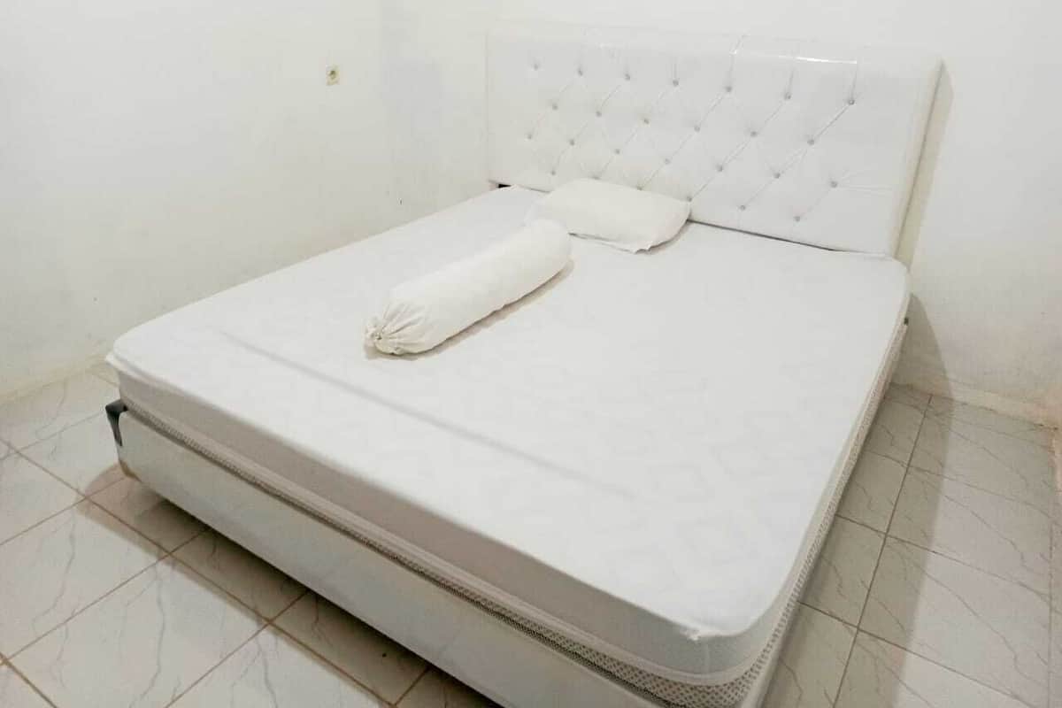 Une chambre avec un lit simple, un matelas blanc, une tête de lit capitonnée et un oreiller blanc.