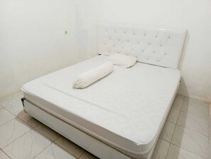 Ein Einzelzimmer mit einem weißen Bett, einer gesteppten Kopfteil und einem weißen Kopfkissen.
