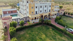 Un edificio grande de varios pisos con un patio central, rodeado de abundante vegetación y una piscina.