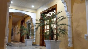 Un pasillo con piso de mármol, arcos blancos y palmeras en macetas.