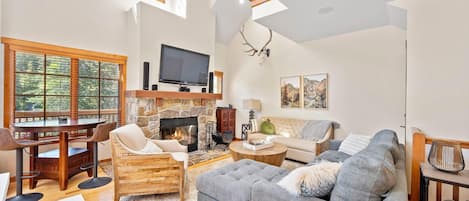 Un salón amplio con chimenea, televisor y ventana grande con vistas a un bosque.