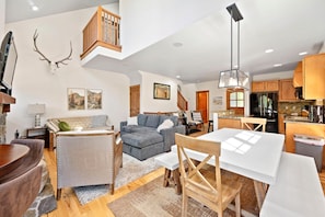 A spacious living area with a high ceiling, a dining table, and a kitchen area with wooden cabinets. - Peaceful Escape | Exclusive Tamarack Perks (Tamarack)