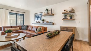 Una sala moderna con una mesa de comedor de madera, un sofá de cuero y estanterías empotradas con objetos decorativos.